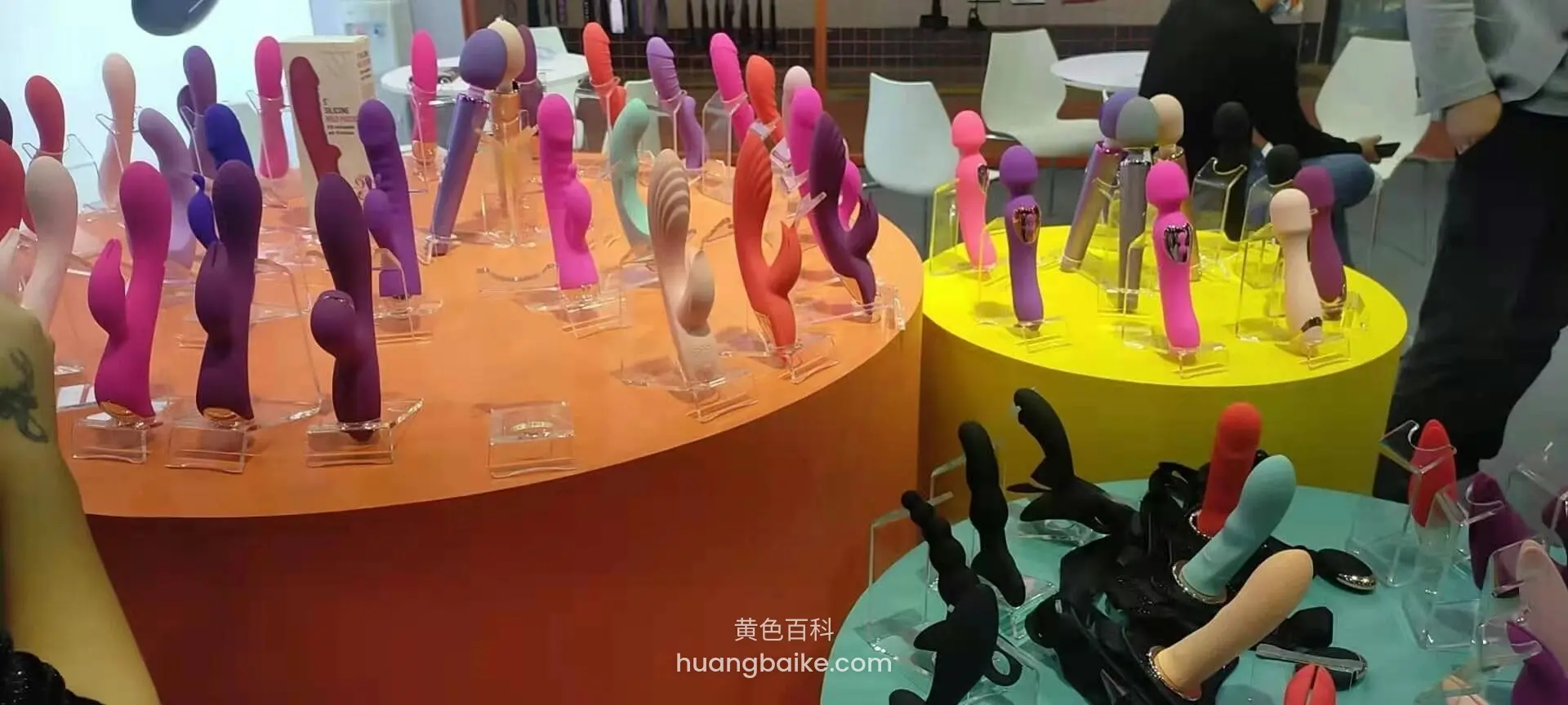 橙色圆台上摆满情趣用品,旁边黄色和蓝色展台也有展示