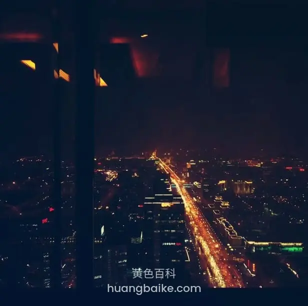 夜景俯瞰城市主干道,车灯连成光河,玻璃窗框挡住部分视线