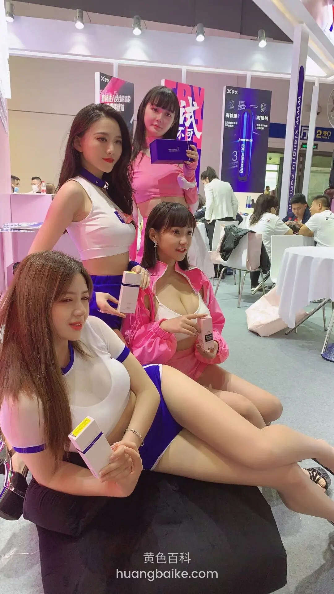 三人坐在黑沙发上,中间一人拿着产品盒子,身后是展会海报
