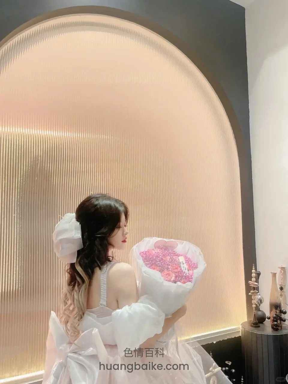 背对镜头抱花束站拱形灯墙前