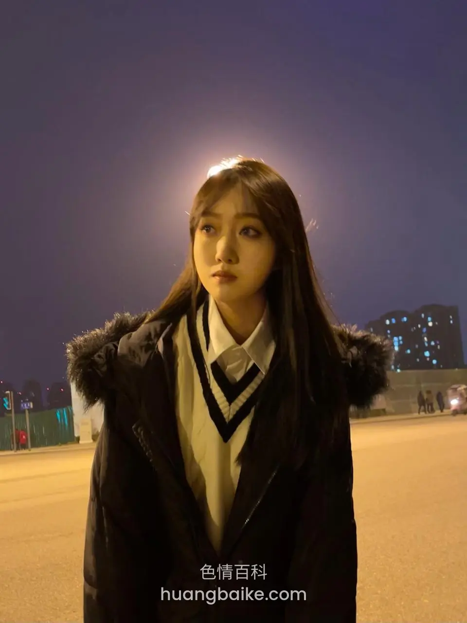 路灯下穿着黑色羽绒服，身后是夜景高楼