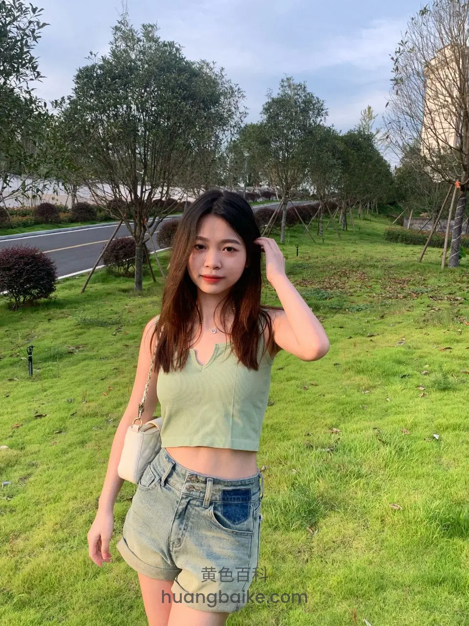 公园草坪上站立，手抬到耳边，身后有路和树
