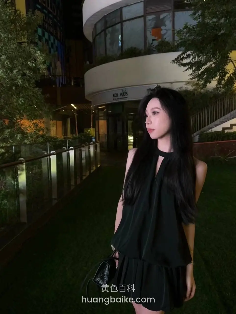 夜里草坪上回头看镜头，手提黑色包，身后是圆形建筑