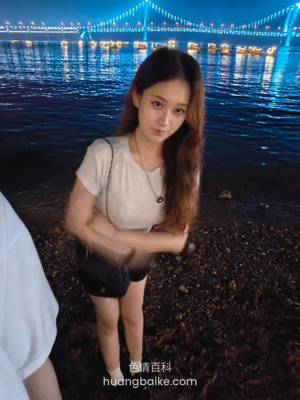 夜晚河边站立，身后亮灯大桥倒映水面