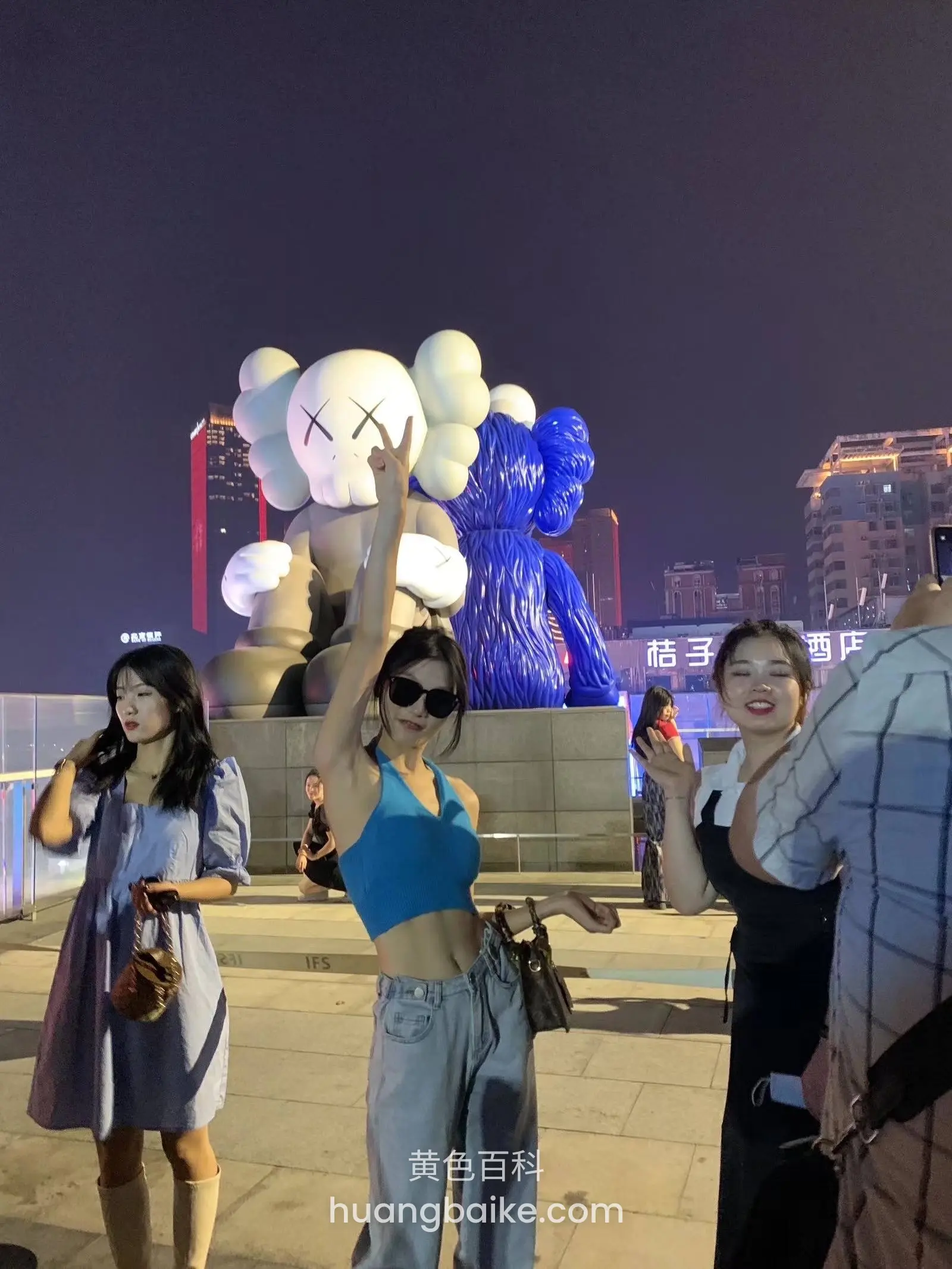 夜里举手对着镜头，身后是KAWS雕塑