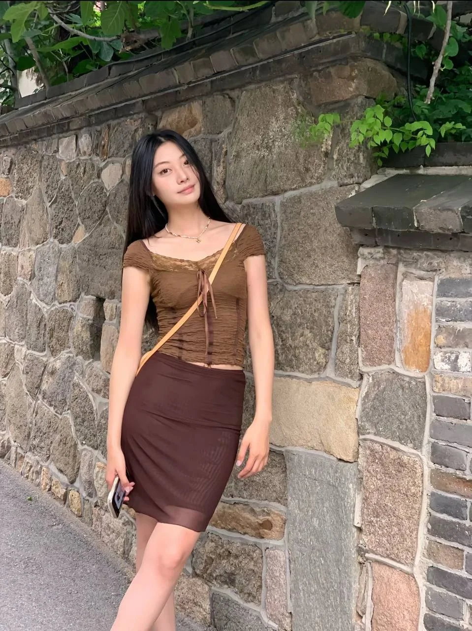 石墙前 女生穿棕色露脐上衣