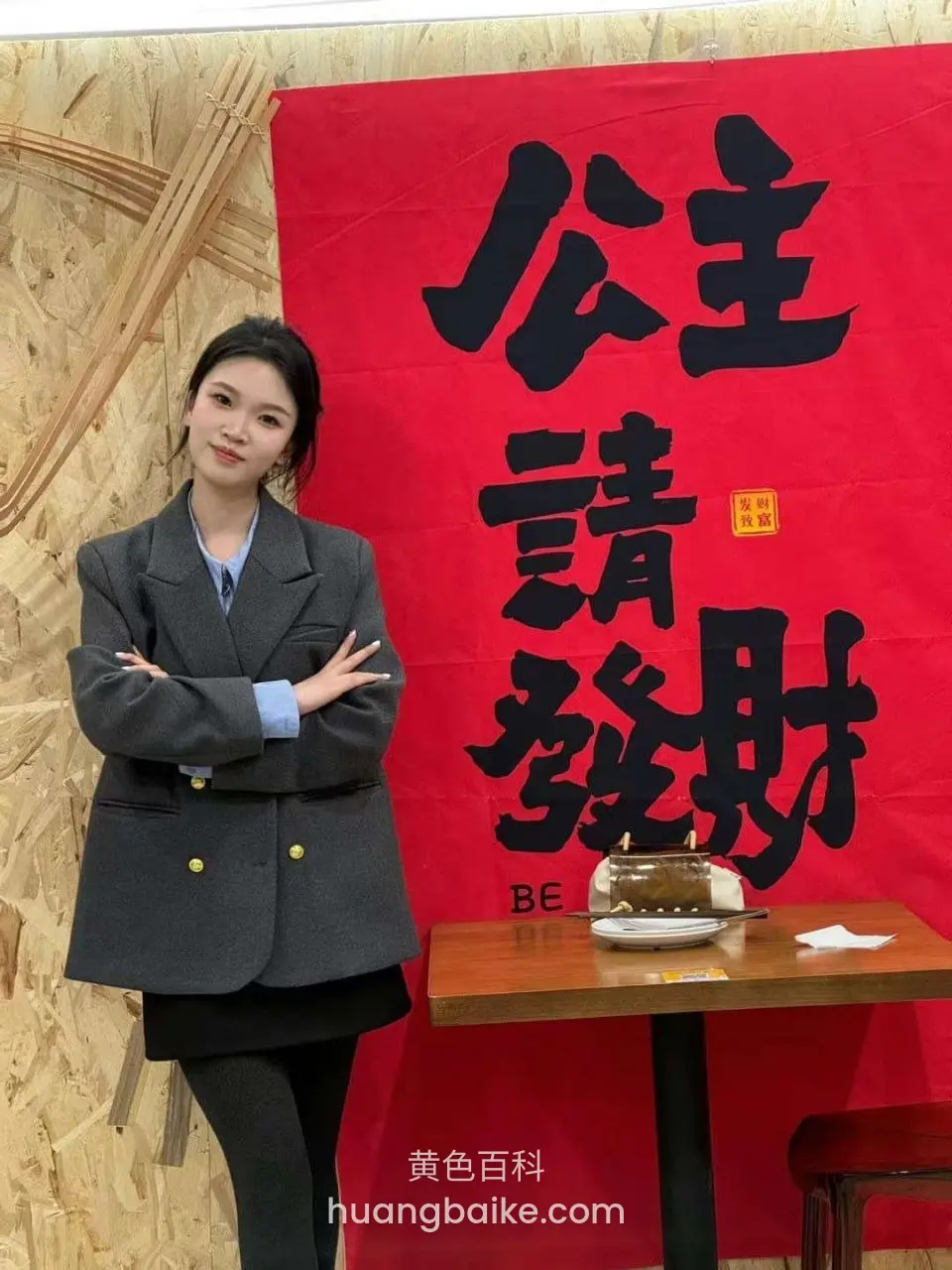 墙前站立抱臂,身后大红旗写着公主请发财