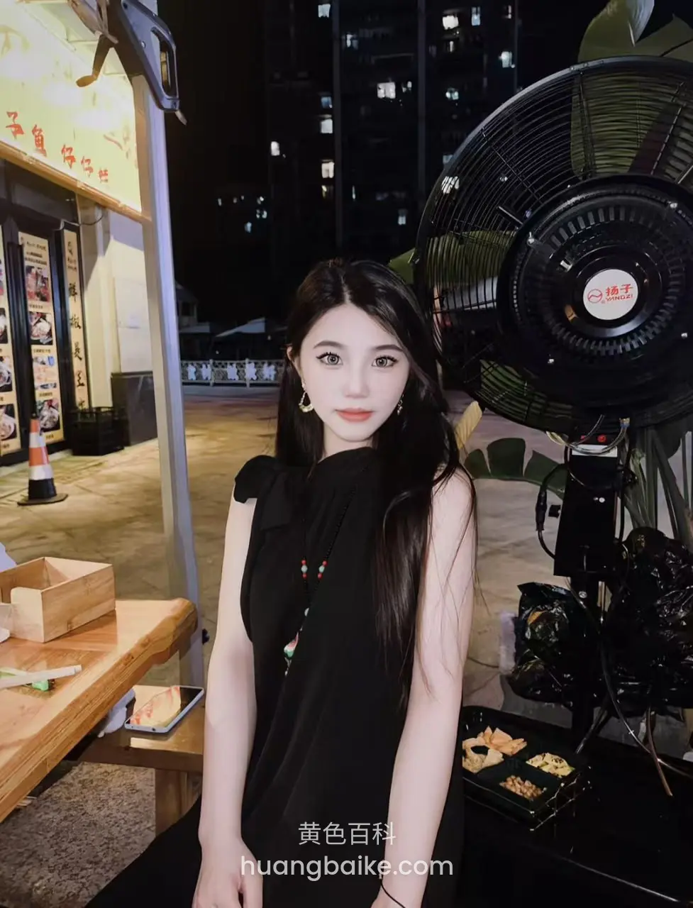 夜市摊前站着，身后有大黑扇和招牌 至尊好仔铺