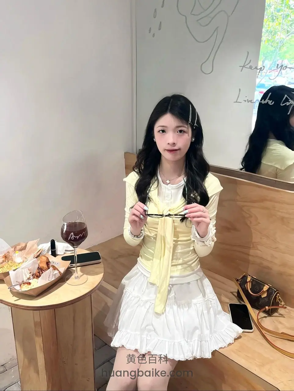拿着眼镜看镜头，桌上红酒和食物