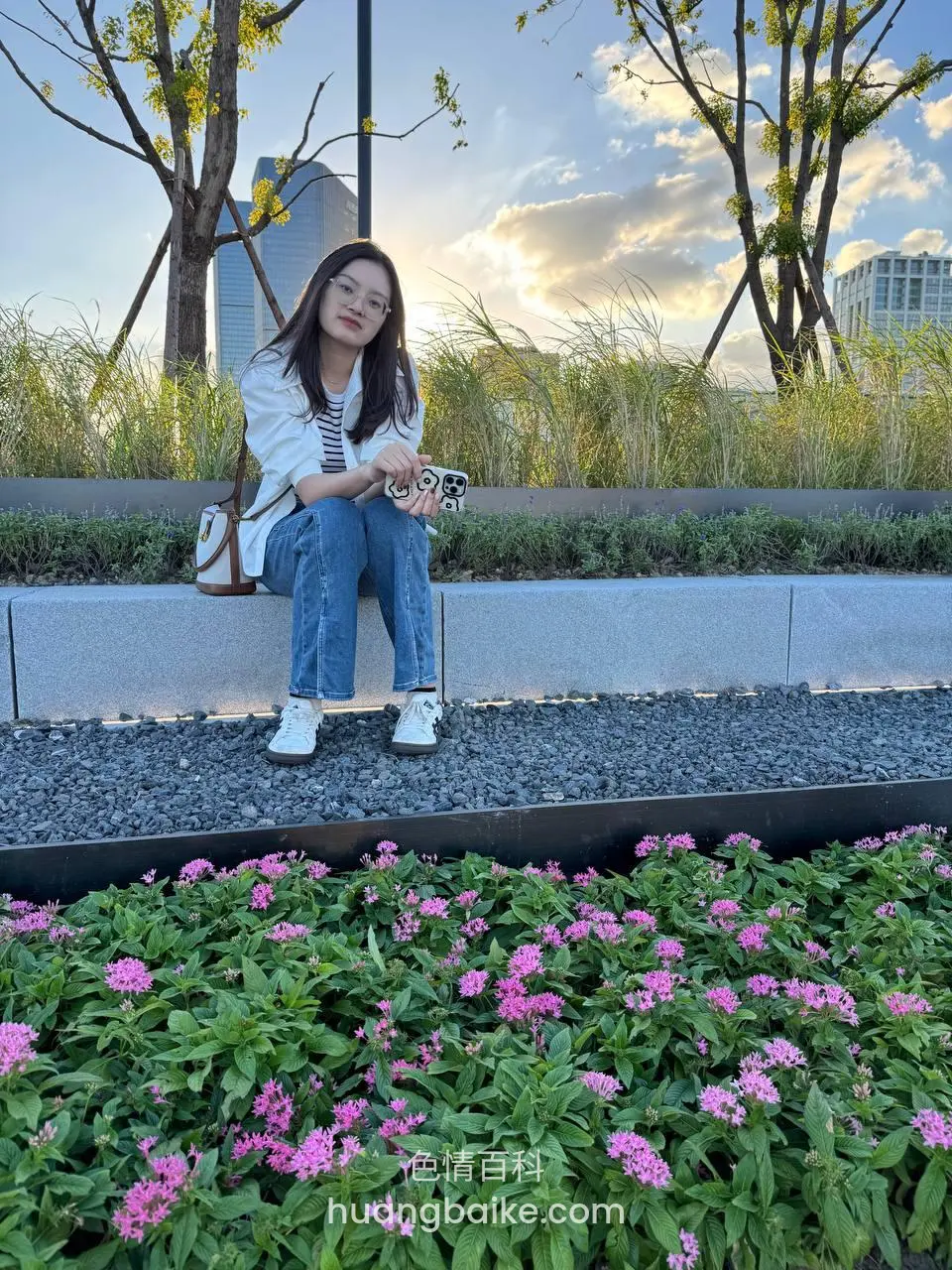 公园花坛边石阶上坐着，镜头对着城市建筑和夕阳