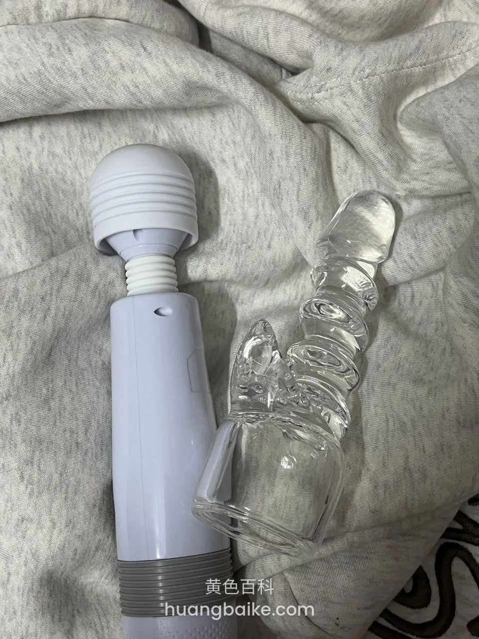 灰色床单上白色按摩棒和玻璃假阳具