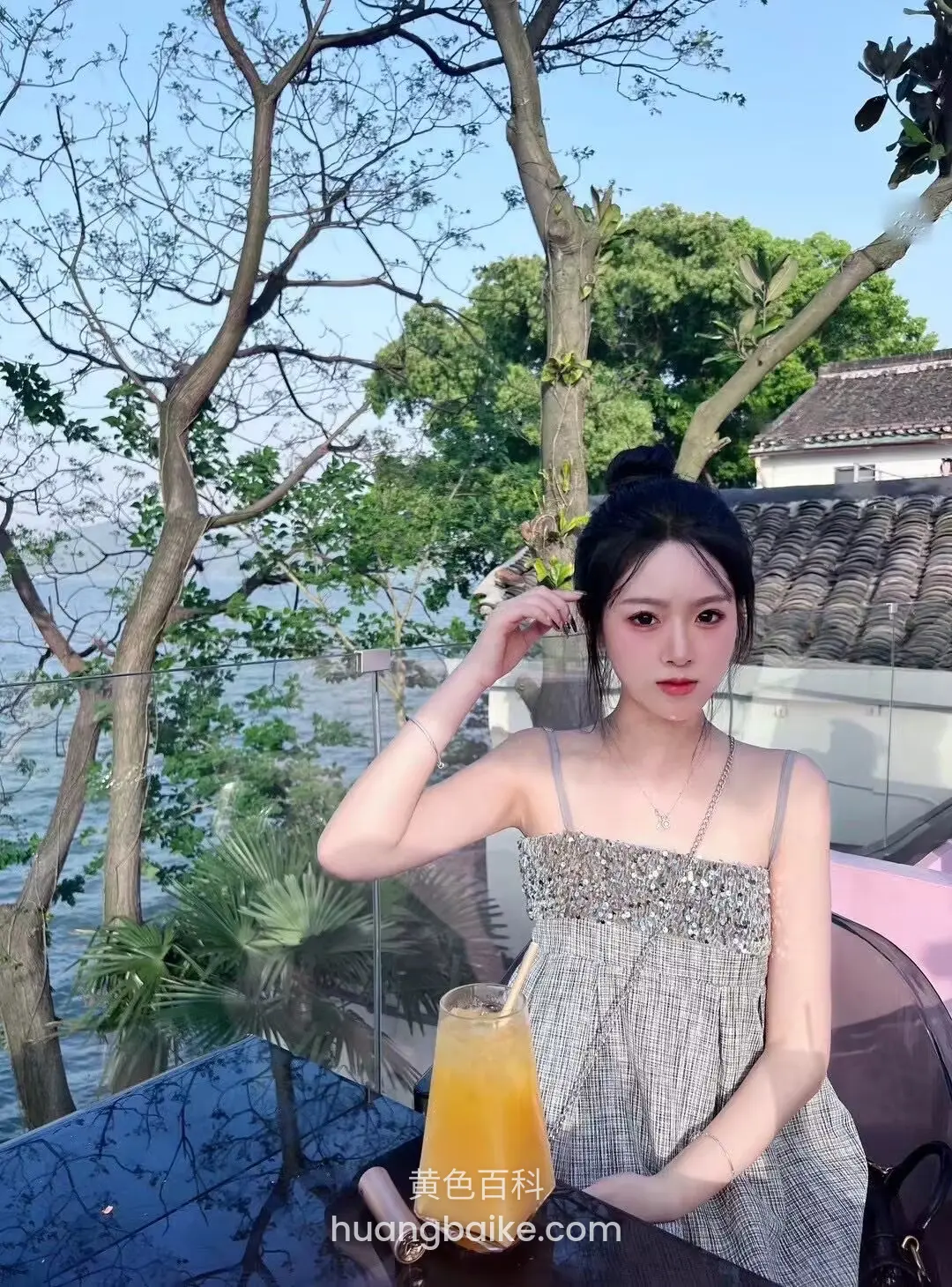 户外餐桌边举杯橙汁，身后是湖和树