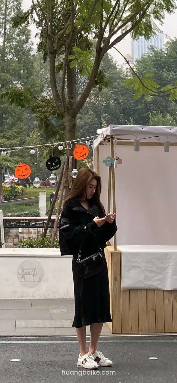 街边树下 低头看手机 旁边挂着南瓜灯