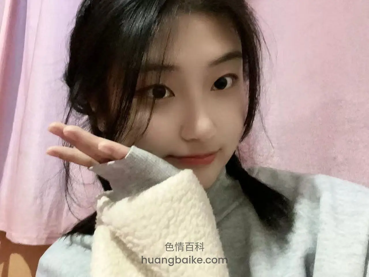 粉色背景前歪头看镜头，手指比心