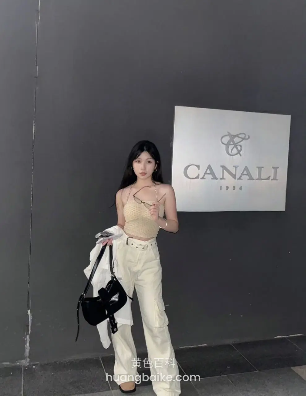 站在灰墙前手拿黑包和白外套，身后是CANALI招牌