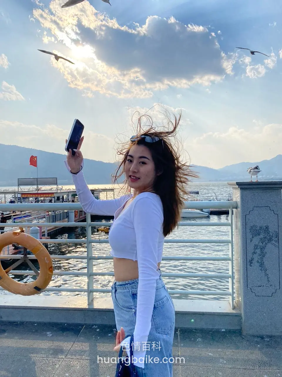 湖边栏杆旁举手机自拍，头发被风吹起