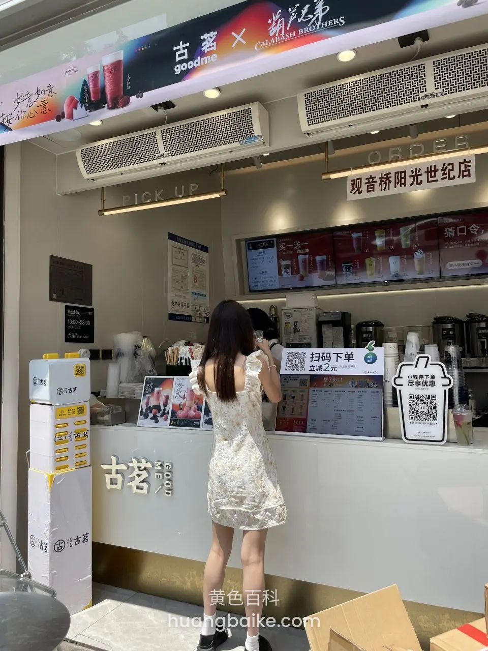 饮料店柜台前站着背对镜头，墙上有古茗和扫码下单