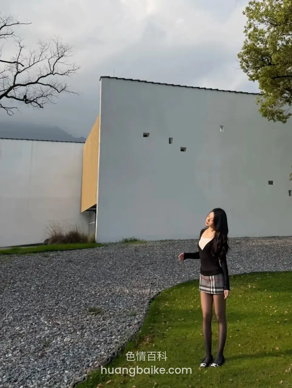 户外建筑前，镜头对着白墙侧身站立手伸向前