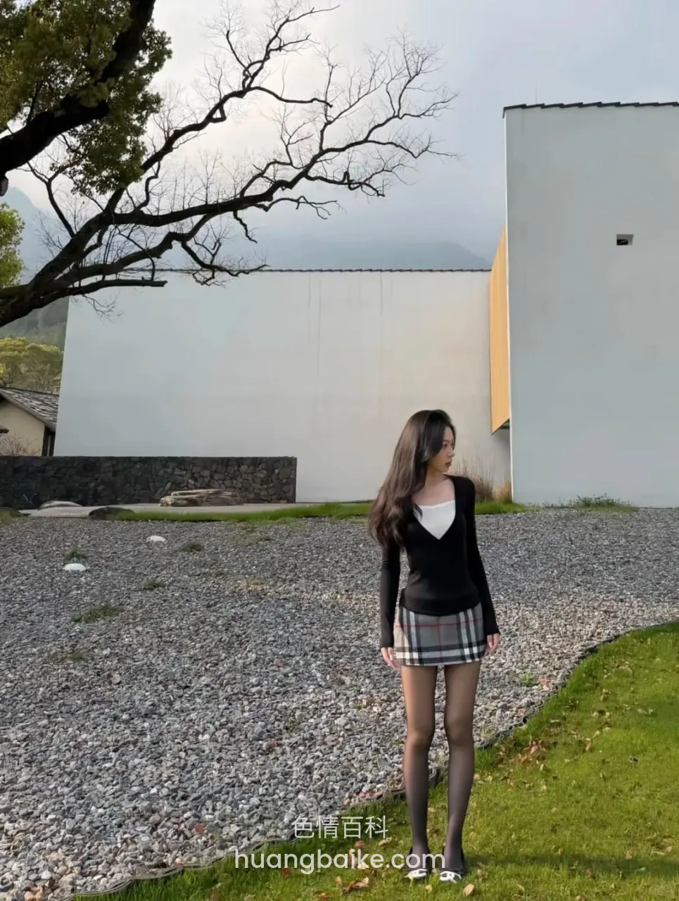 户外白墙建筑旁，站在草地和碎石地上回头看