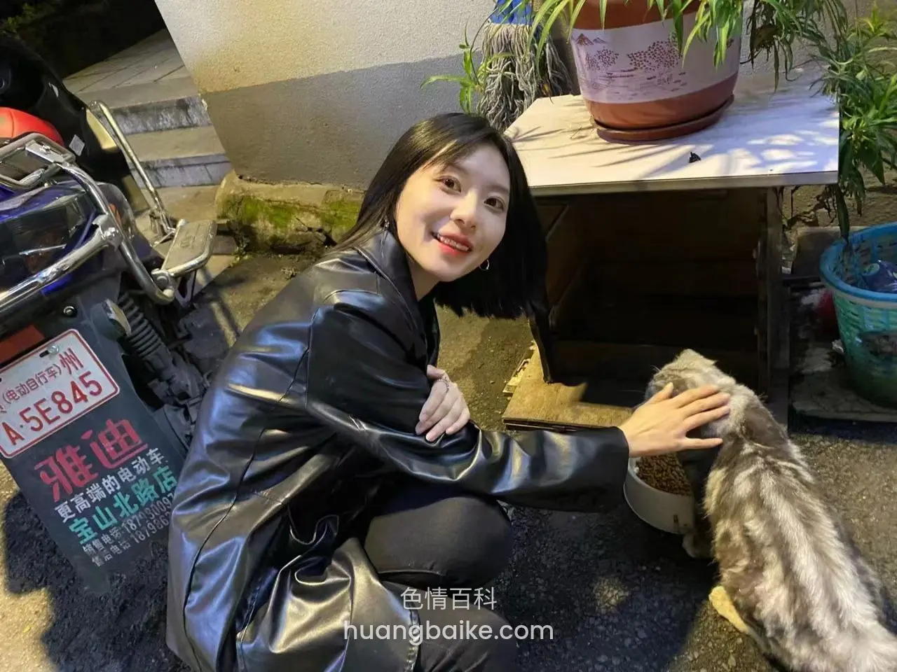 户外蹲在电动车旁伸手摸猫，旁边有招牌