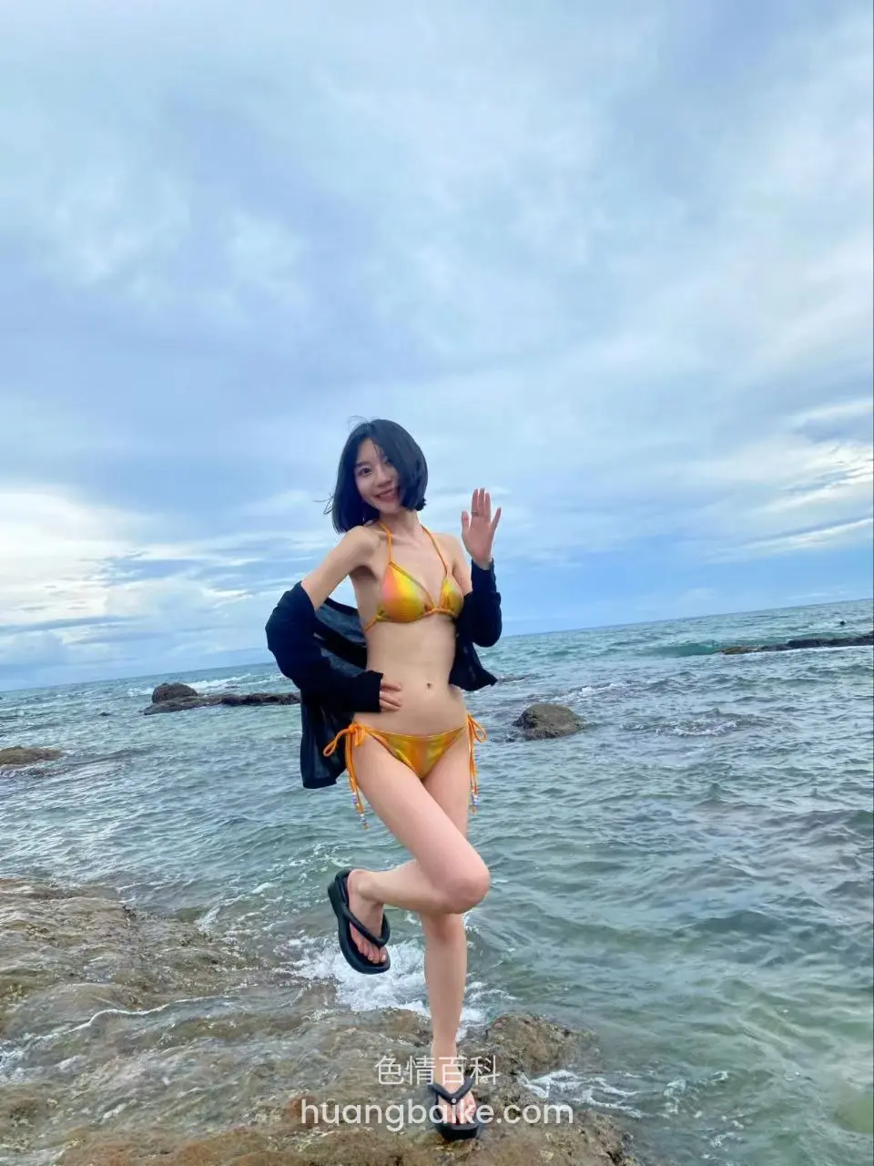 海边岩石上单脚站立，左手比耶
