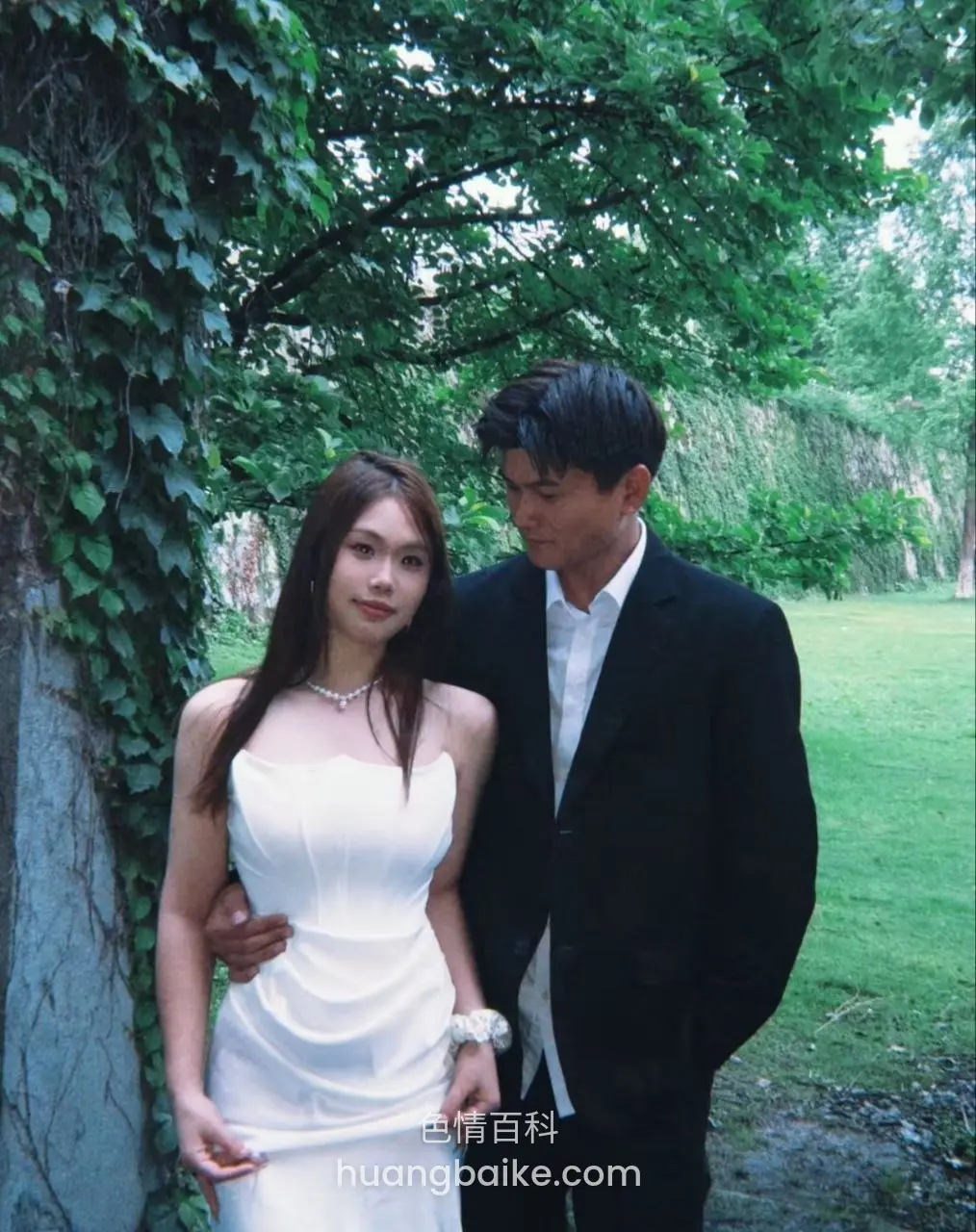户外绿树下，男人搂着她腰低头看