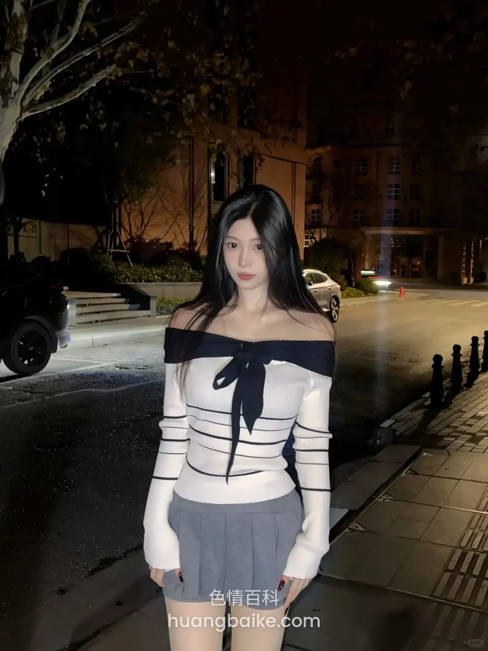 夜晚路边站立，身后是建筑和街道