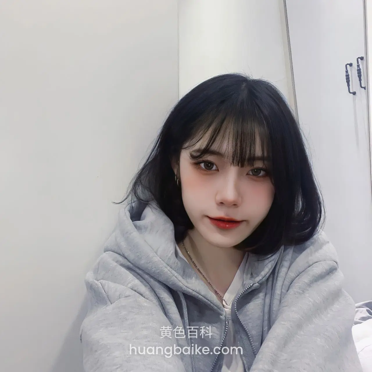 卧室白墙前，灰色卫衣低头看镜头
