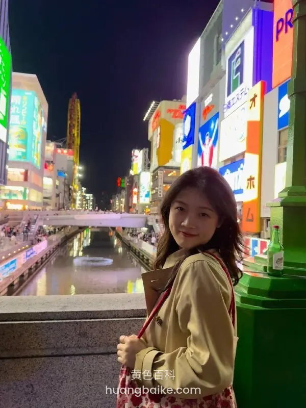 夜里街头回头看镜头，手里拿着包，身后河边霓虹招牌