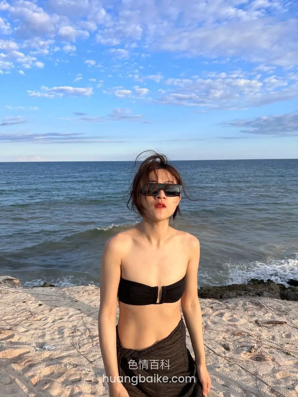 海边站着看镜头，身后是海浪和蓝天