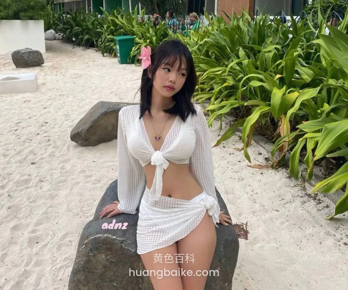 坐在沙滩大石头上，身后是绿植和建筑