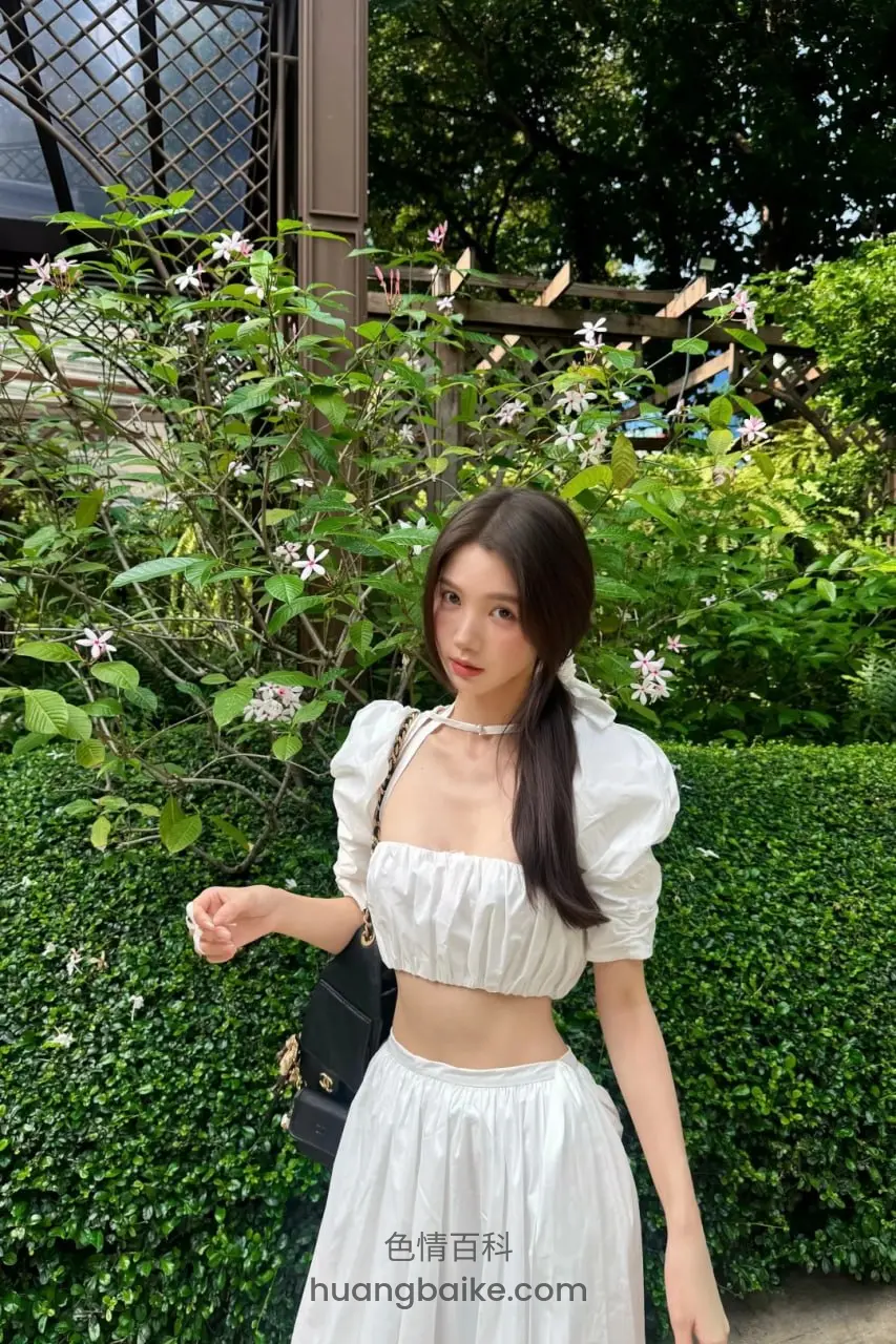 花园绿植前站立，左手提黑包右手握着什么