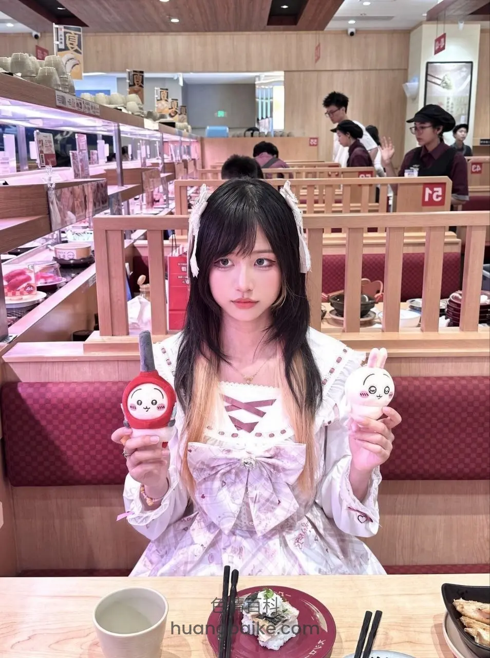 餐厅里拿着两只饭团玩偶，桌上摆着寿司