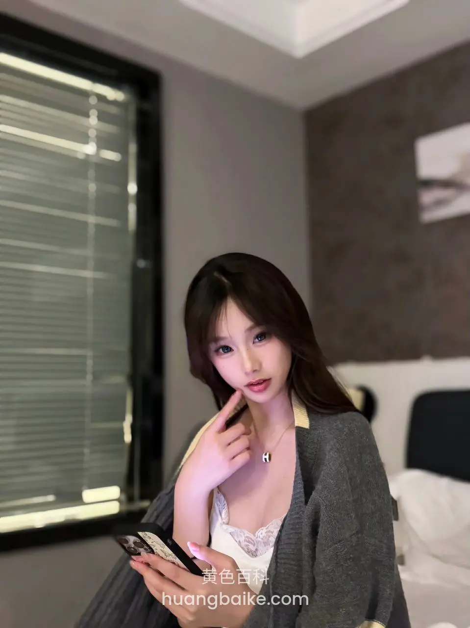 卧室里拿着手机看镜头，手指点着下巴