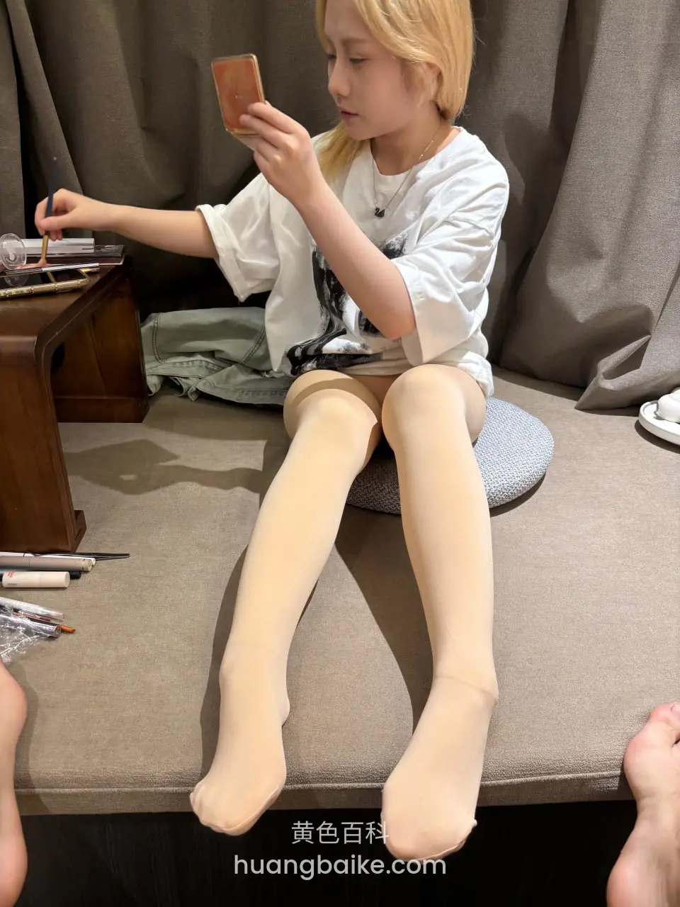 坐在垫子上看手机，桌上散落化妆品