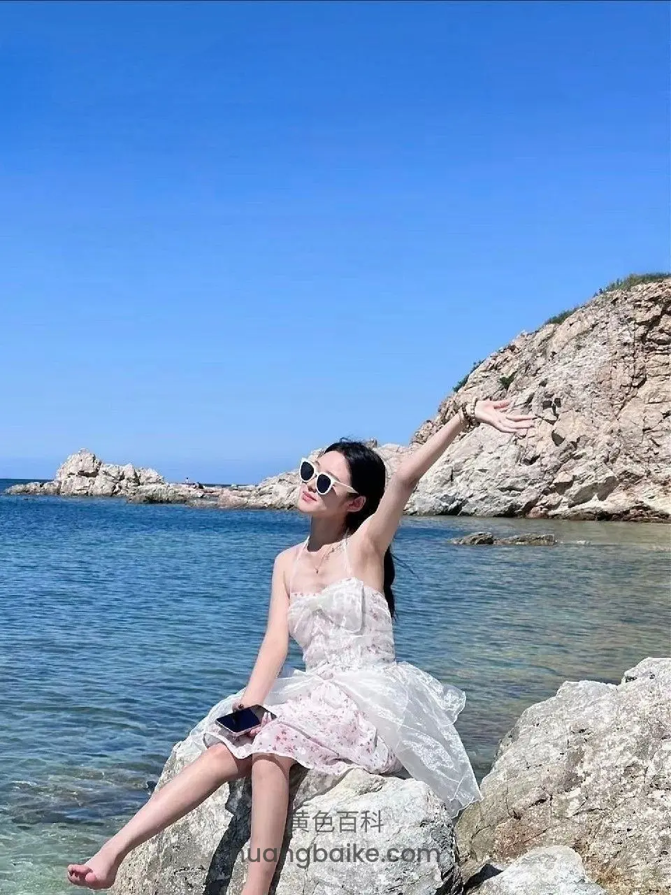 海边岩石上坐着举手，手机在腿上