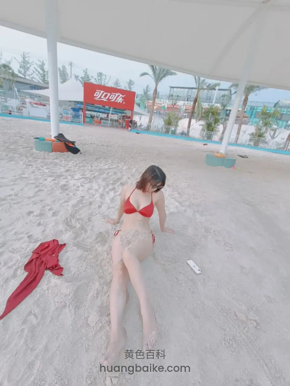 红比基尼女子跪坐在沙滩 身后红招牌