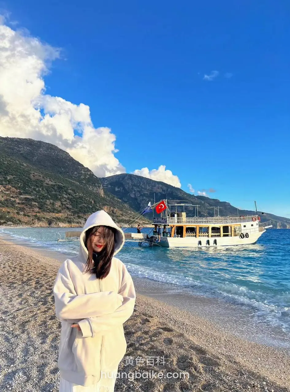 沙滩上站着双手抱胸，身后是土耳其国旗游船
