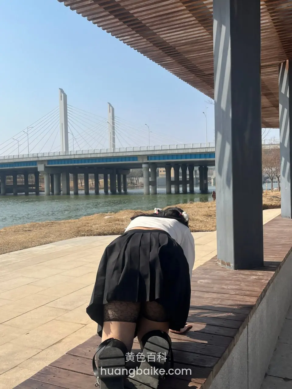 户外木板上跪着，身后是河上大桥