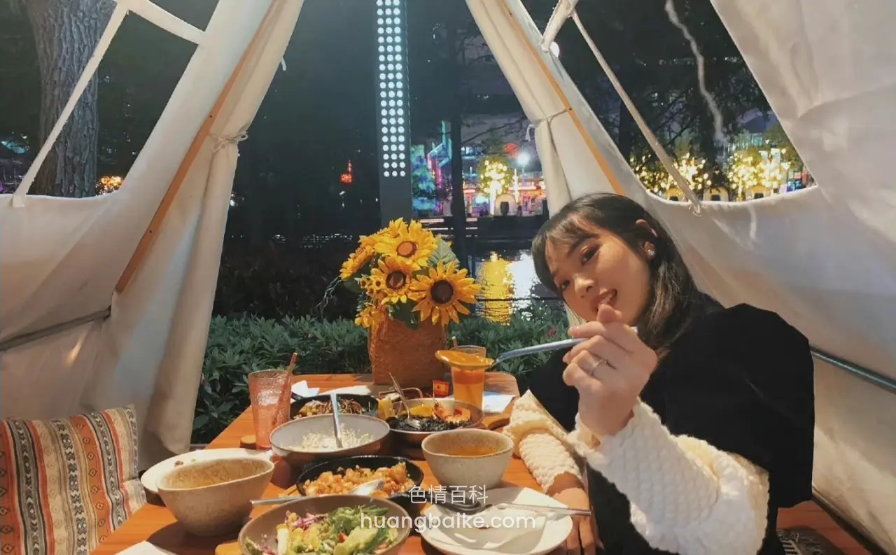 帐篷里夜景餐桌前拿着筷子看镜头，桌上满是食物
