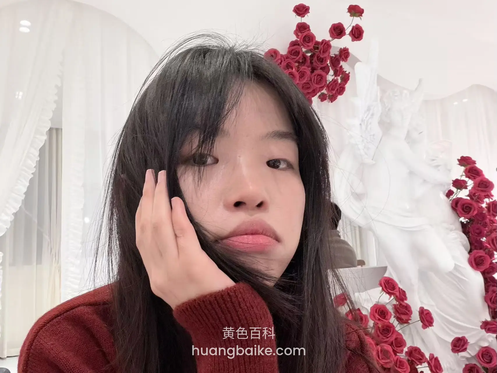 手托着脸看镜头，身后白色天使雕像和红玫瑰