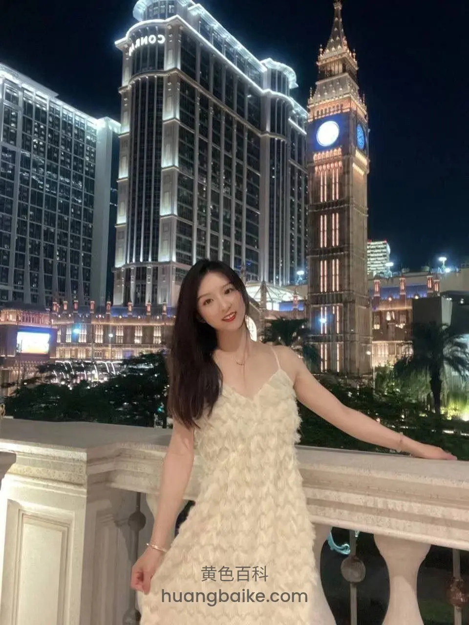 夜景阳台扶栏摆姿势，身后的酒店和钟楼亮着灯