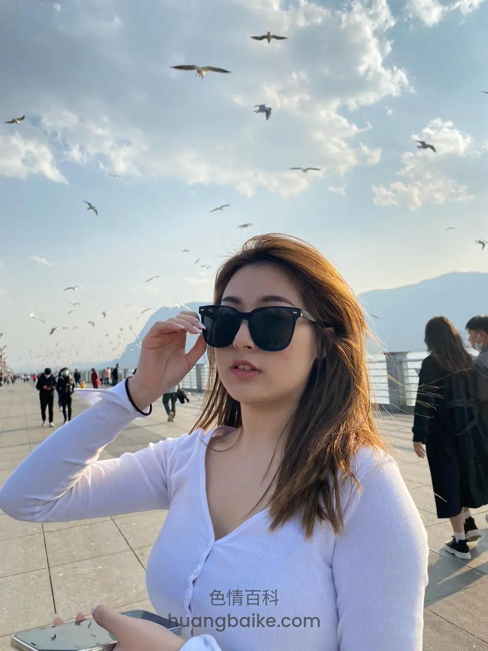 码头人群中摘下墨镜看镜头，手里拿着手机