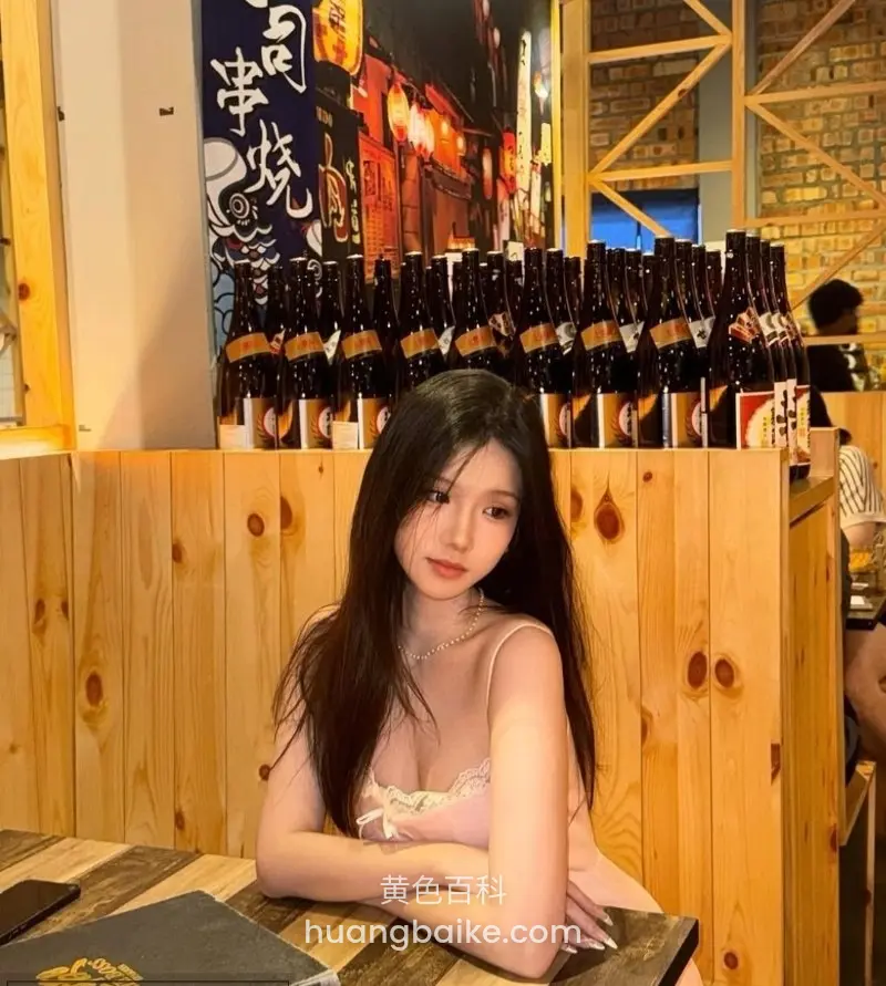 坐在木桌前双手交叉，身后一排啤酒瓶和日式招牌