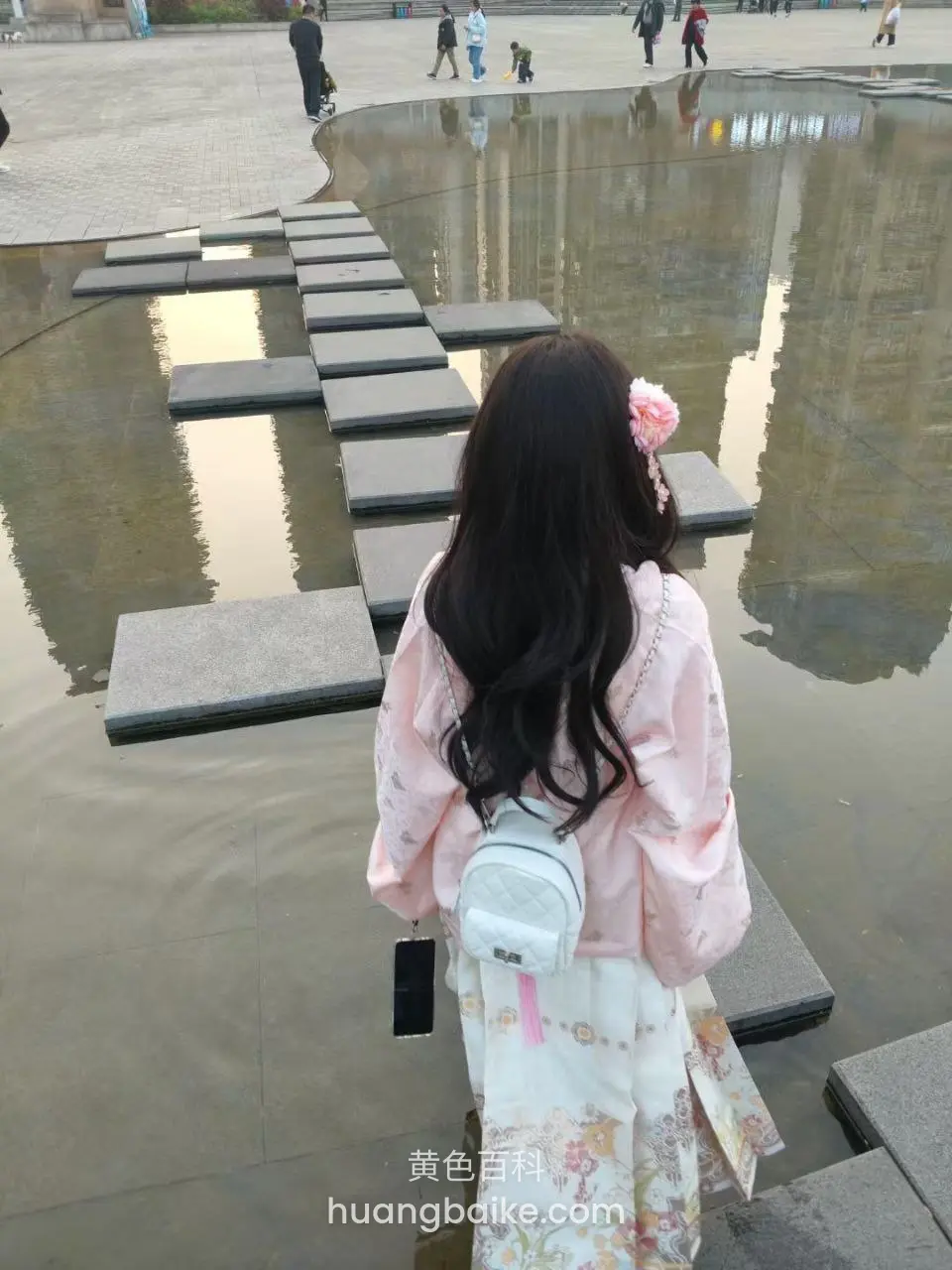 水上石板路背对镜头走着，包上挂着手机