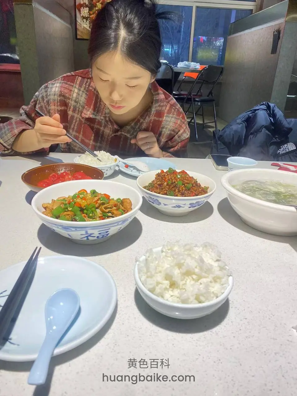 拿着筷子低头吃桌上的菜和米饭