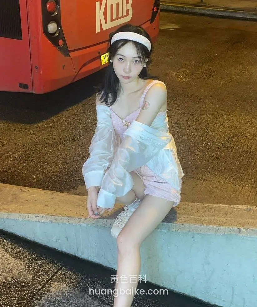 路边水泥墩上坐着，看向镜头，身后红色KMB公交车