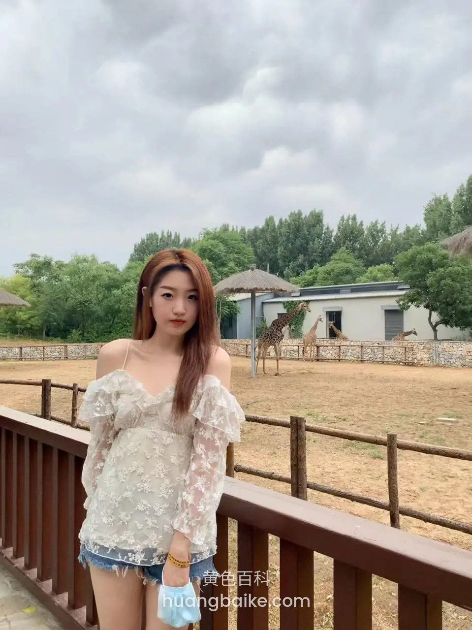 动物园围栏前站立，手里拿着蓝色口罩