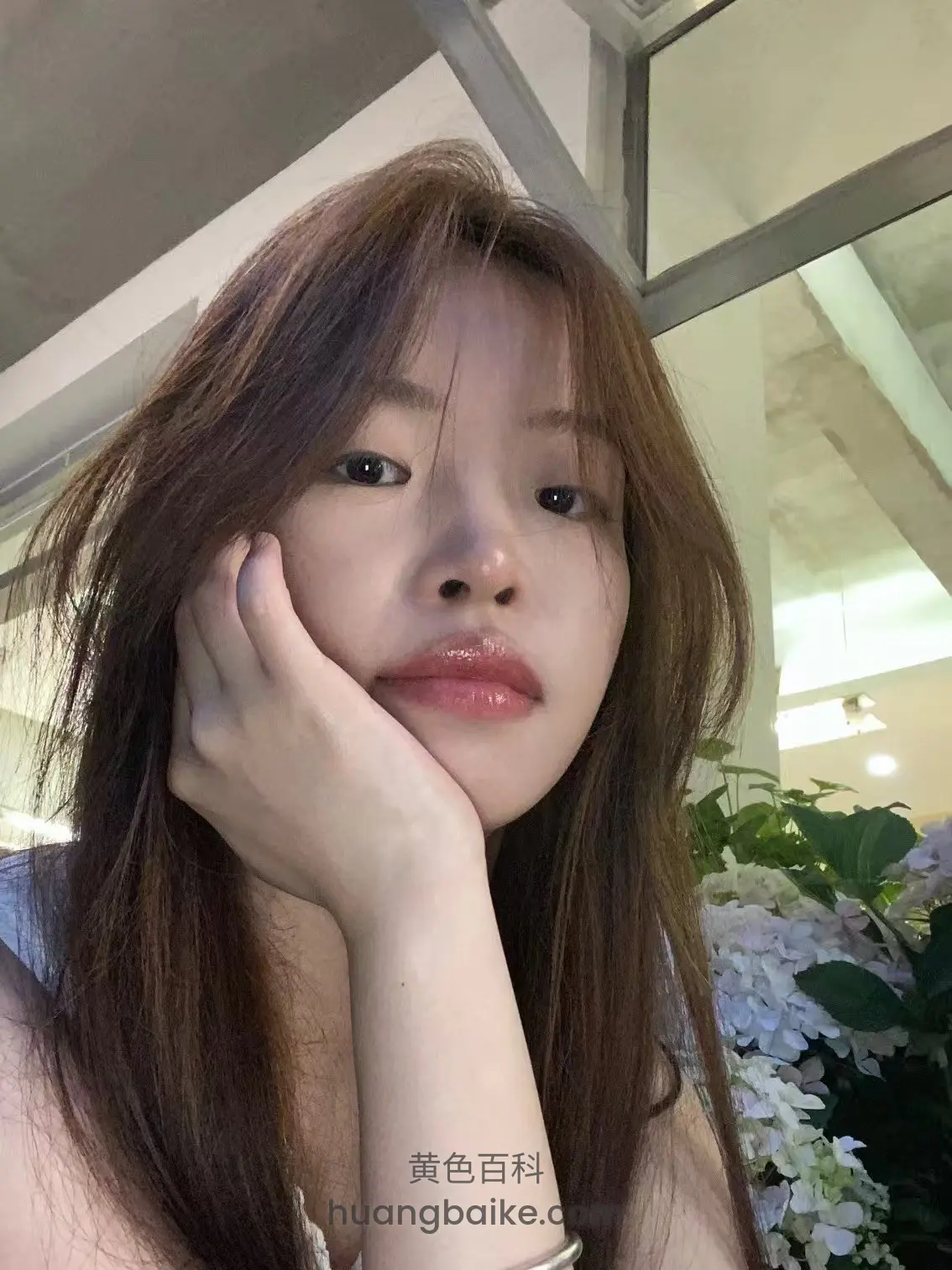 手托着脸自拍，身后是花丛和玻璃窗