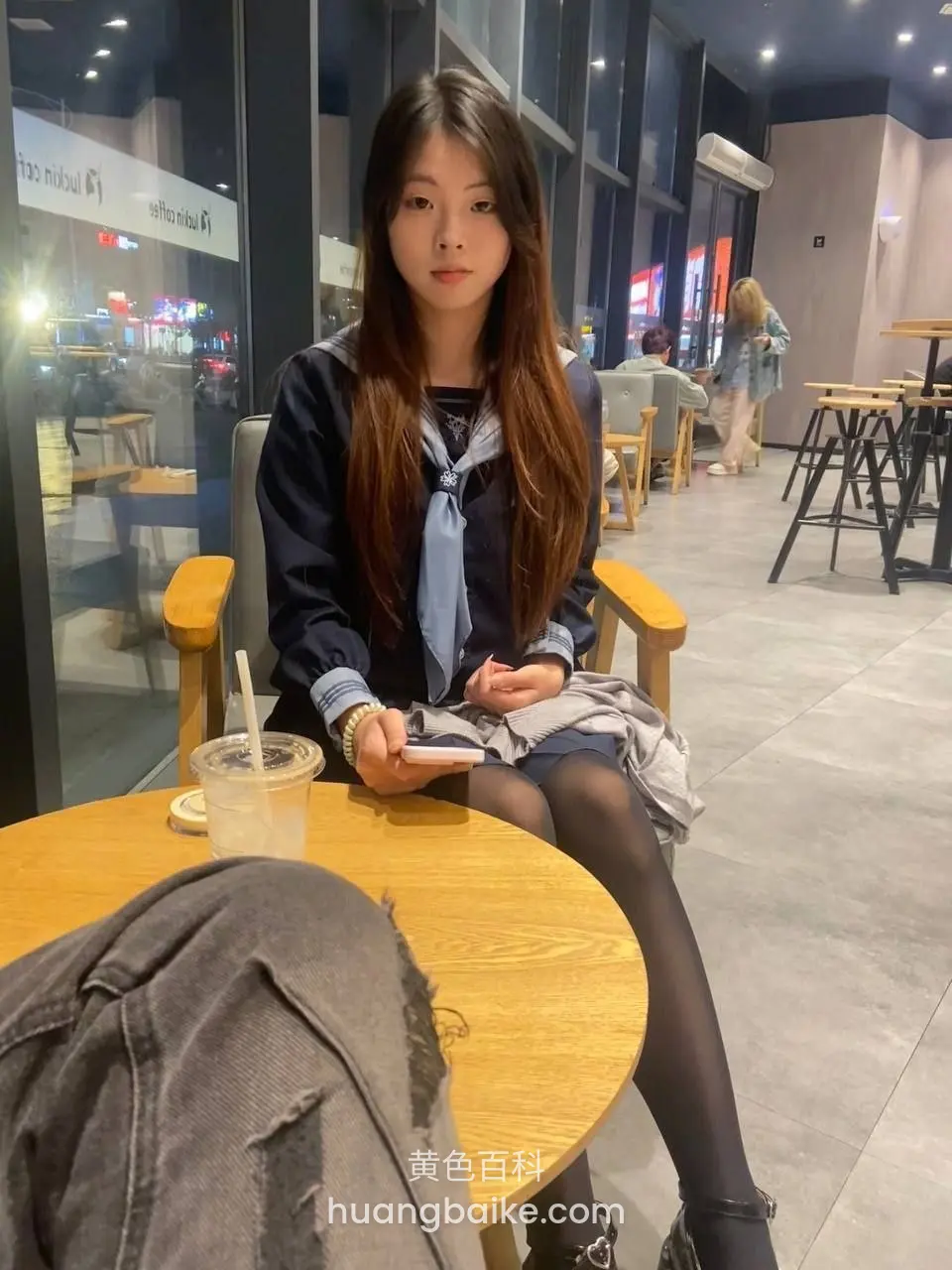 咖啡店木桌前拿着手机，身后玻璃门写着 m stand